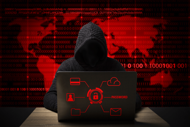 Hacker i en jakke med hætte med en bærbar computer sidder ved bordet