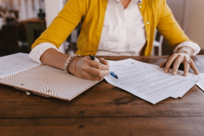 Kvinde i gul blazer skriver på et stykke papir