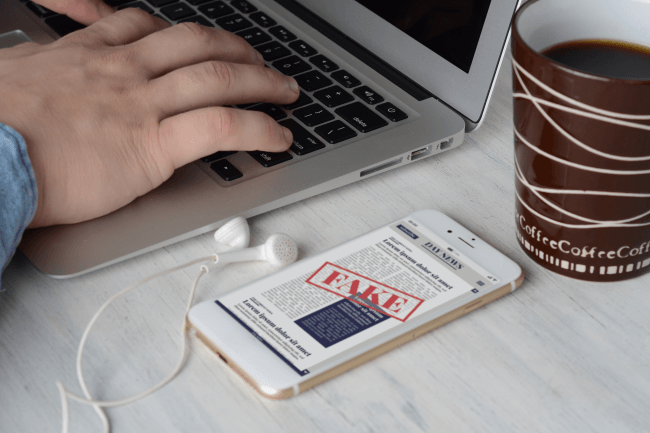 Forretningsmand på tastaturet med kop kaffe og digitale falske nyheder på smartphone